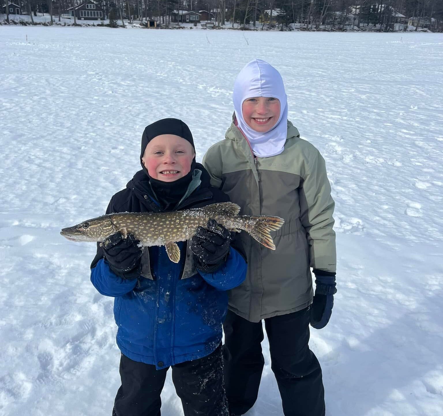 Two anglers on the ice holding a large fish