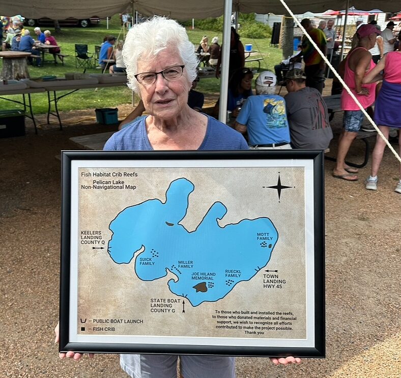 Woman at an event tent displaying a framed map of Pelican Lake